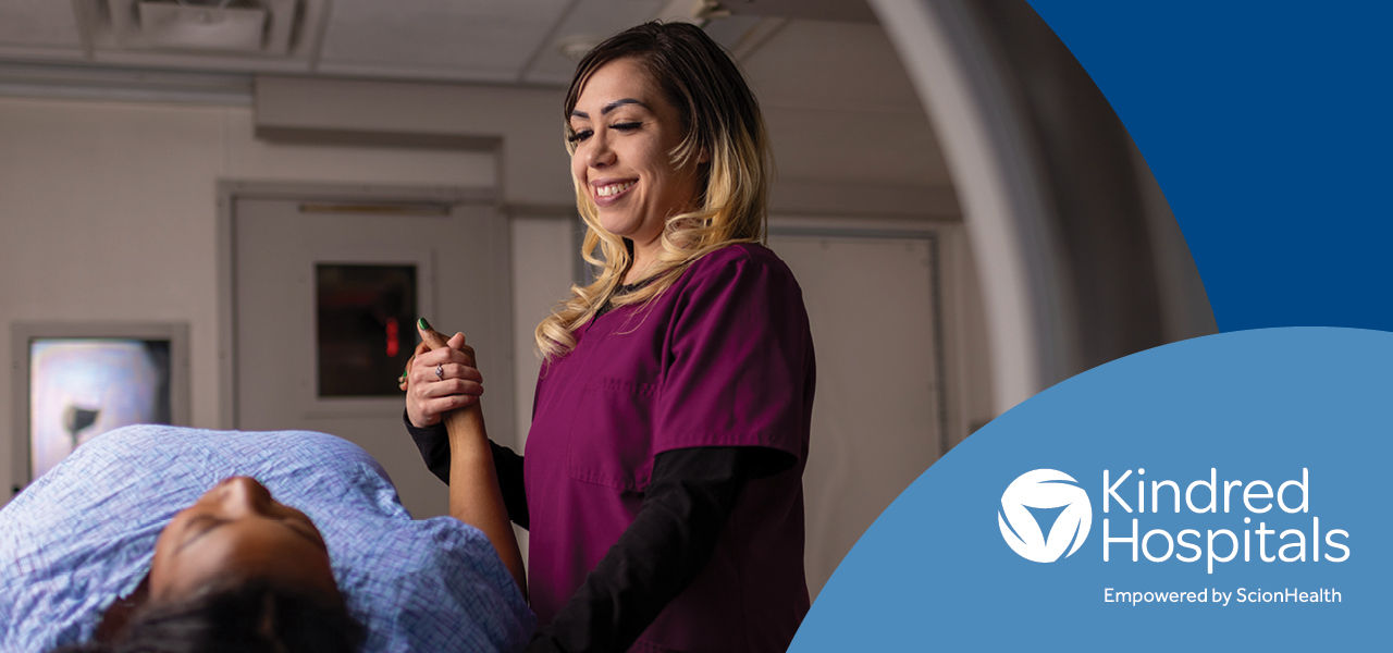 nurse in scrubs holding the hand of a prone patient entering an MRI machine. Kindred Hospitals logo bottom right