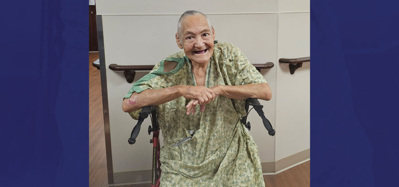 Kindred Hospital San Antonio patient Ofelia smiles while sitting in her walker in the hospital hallway